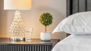 Habitación de hotel impecable con una cama, una lámpara de noche, una pequeña planta en maceta y una obra de arte enmarcada en la pared.