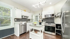 Una cocina moderna con armarios blancos, una isla central, electrodomésticos de acero inoxidable y un salpicadero blanco y negro.