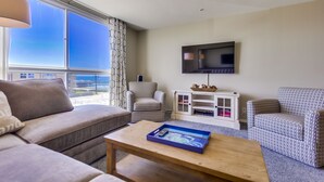 A living room with a sofa, armchairs, a coffee table, a TV, and a view of the outdoors.