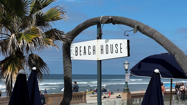 A beach house sign with palm trees and a view of the ocean.