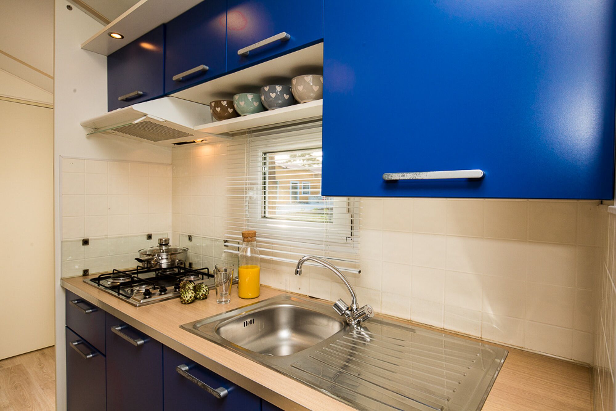 A modern kitchen with blue cabinets, a stainless steel sink, and a window with blinds.