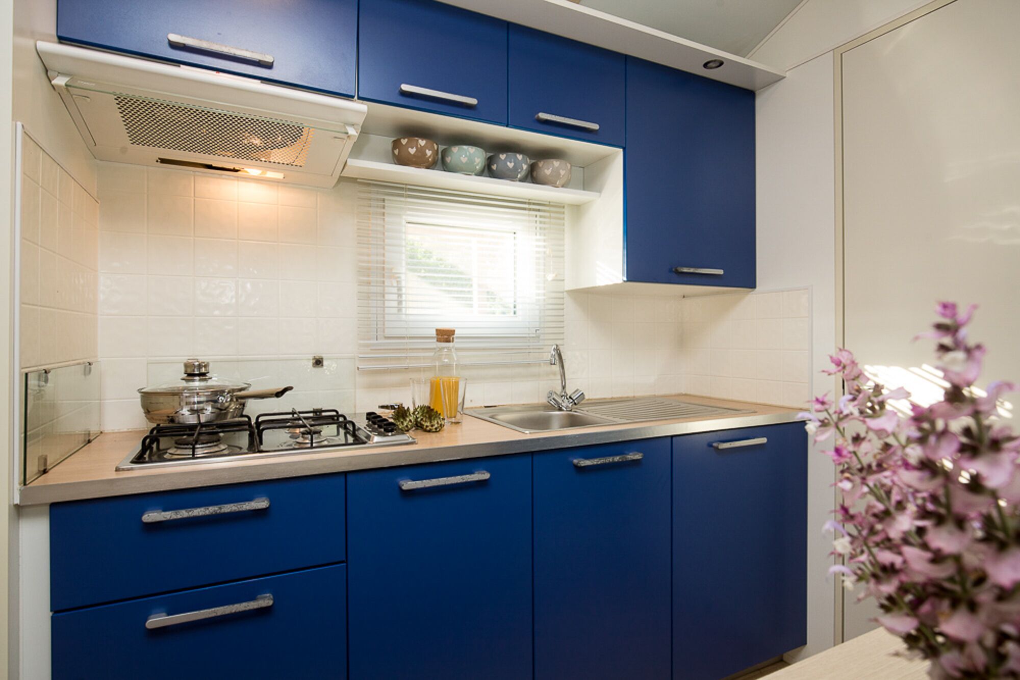 Une cuisine moderne avec des meubles bleus, une cuisinière à gaz et une fenêtre équipée de stores.