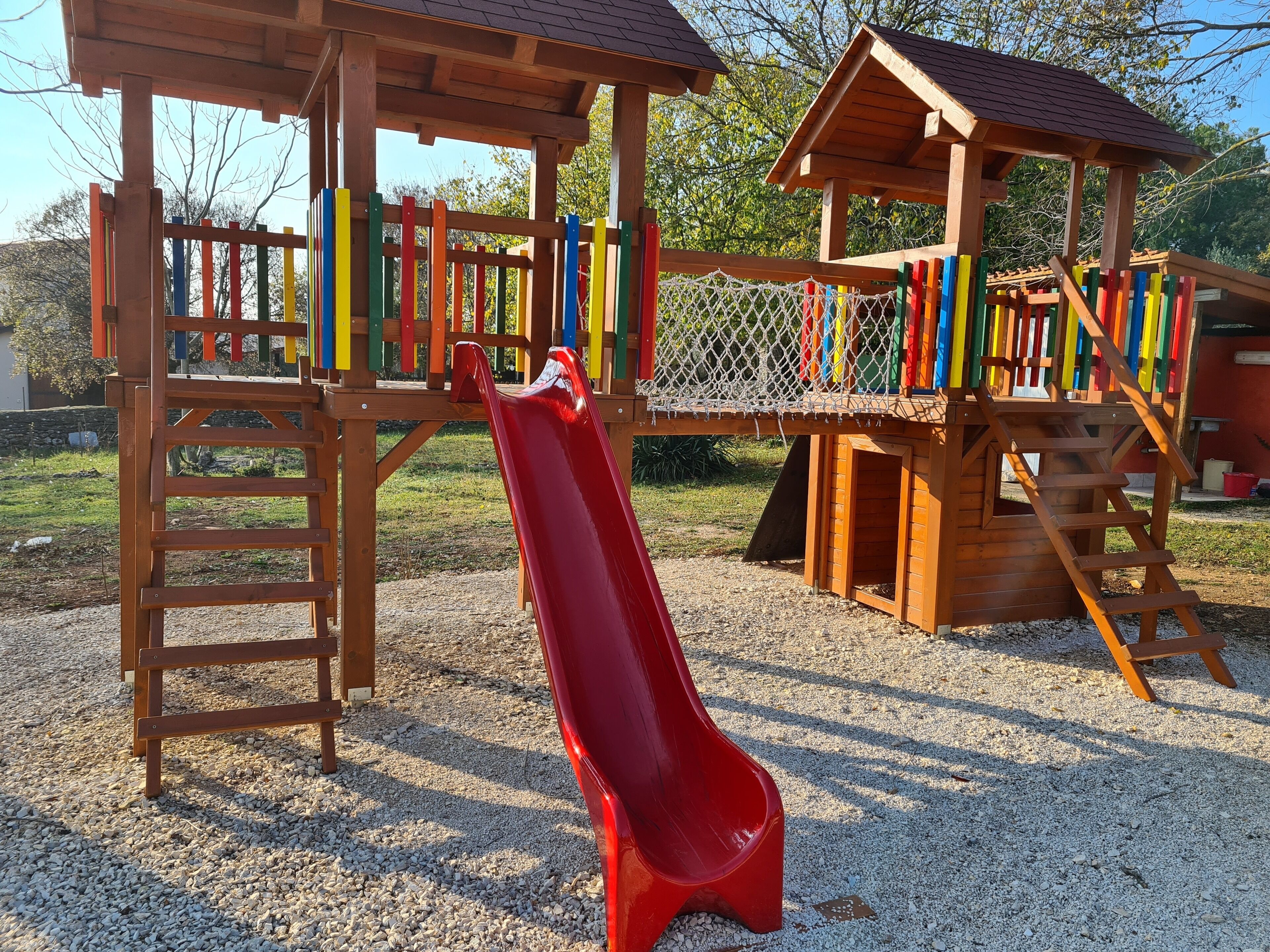 A wooden playground with a red slide and climbing structures.