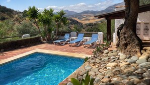 Una piscina con agua azul, rodeada de sillas de descanso y vistas a montañas.