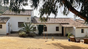 Un edificio tradicional con tejado de baldosas, pared de piedra y un patio con mobiliario exterior.