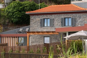 Ein Steinhaus mit rotem Ziegeldach, einem Balkon mit Stühlen und einem Holzzaun.