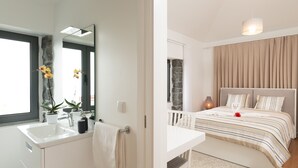 A modern bathroom with a large mirror, sink, and potted plants. The bedroom features a bed with striped bedding, a bedside table, and a lamp. - BHF Residences Ying Yang (Calheta)