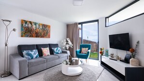 A modern living room with a grey sofa, a round coffee table, a blue armchair, a flat-screen TV, and a large window. - BHF Residences Ying Yang (Calheta)