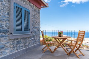 Ein Steingebäude mit blauen Fensterläden, einem Balkon mit Tisch und Stühlen sowie Blick auf das Meer.