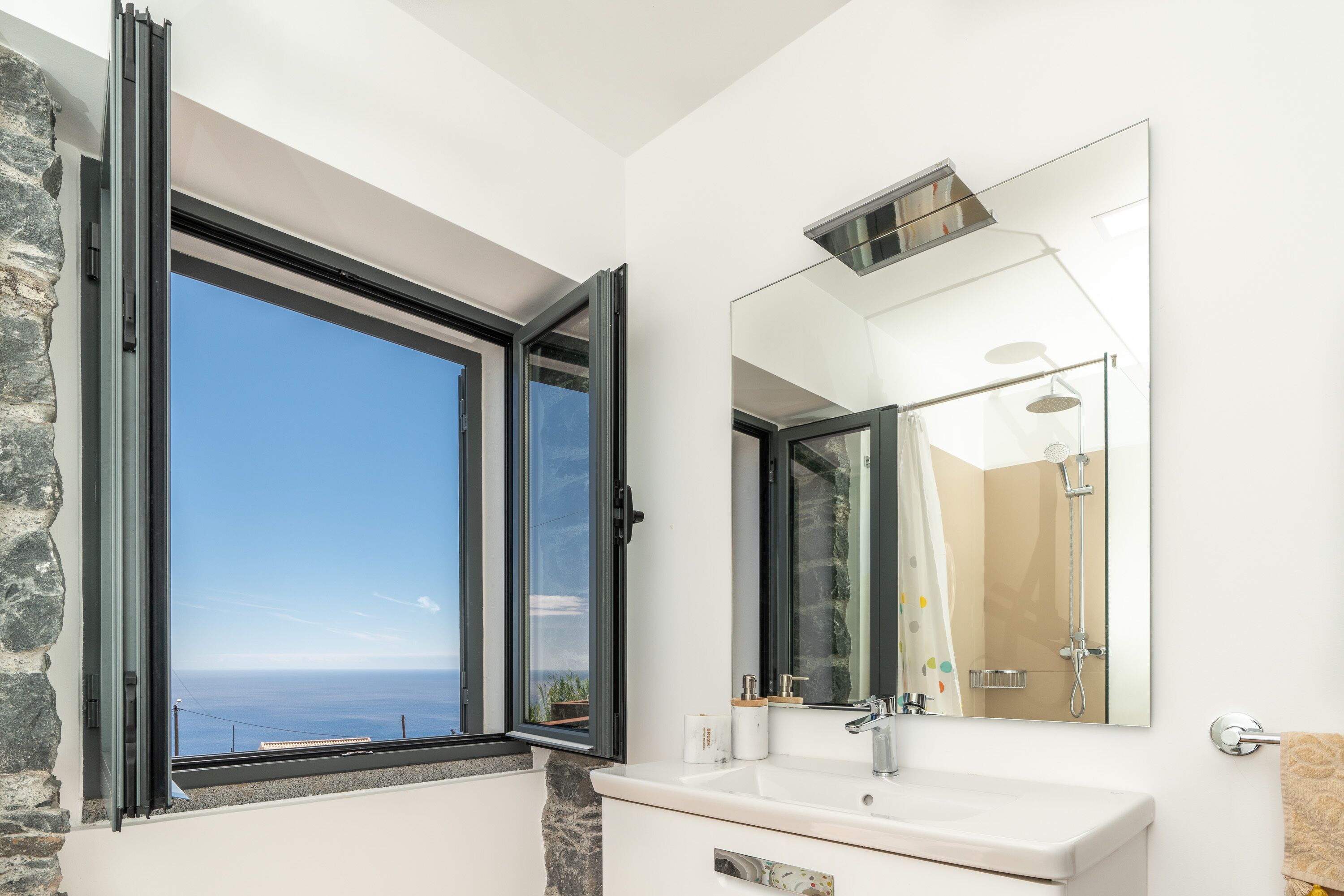 Un bagno con un'ampia finestra, un lavandino, uno specchio e una doccia.