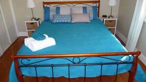 Una cama bien tendida con cubrecama y almohadas azules, un cabecero de madera y dos mesitas de noche con lámparas y un reloj.