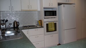 Una cocina con armarios blancos, estufa a gas, microondas, horno y refrigerador.