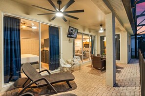 A hotel room with a bed, a TV, and a balcony with chairs and a table.