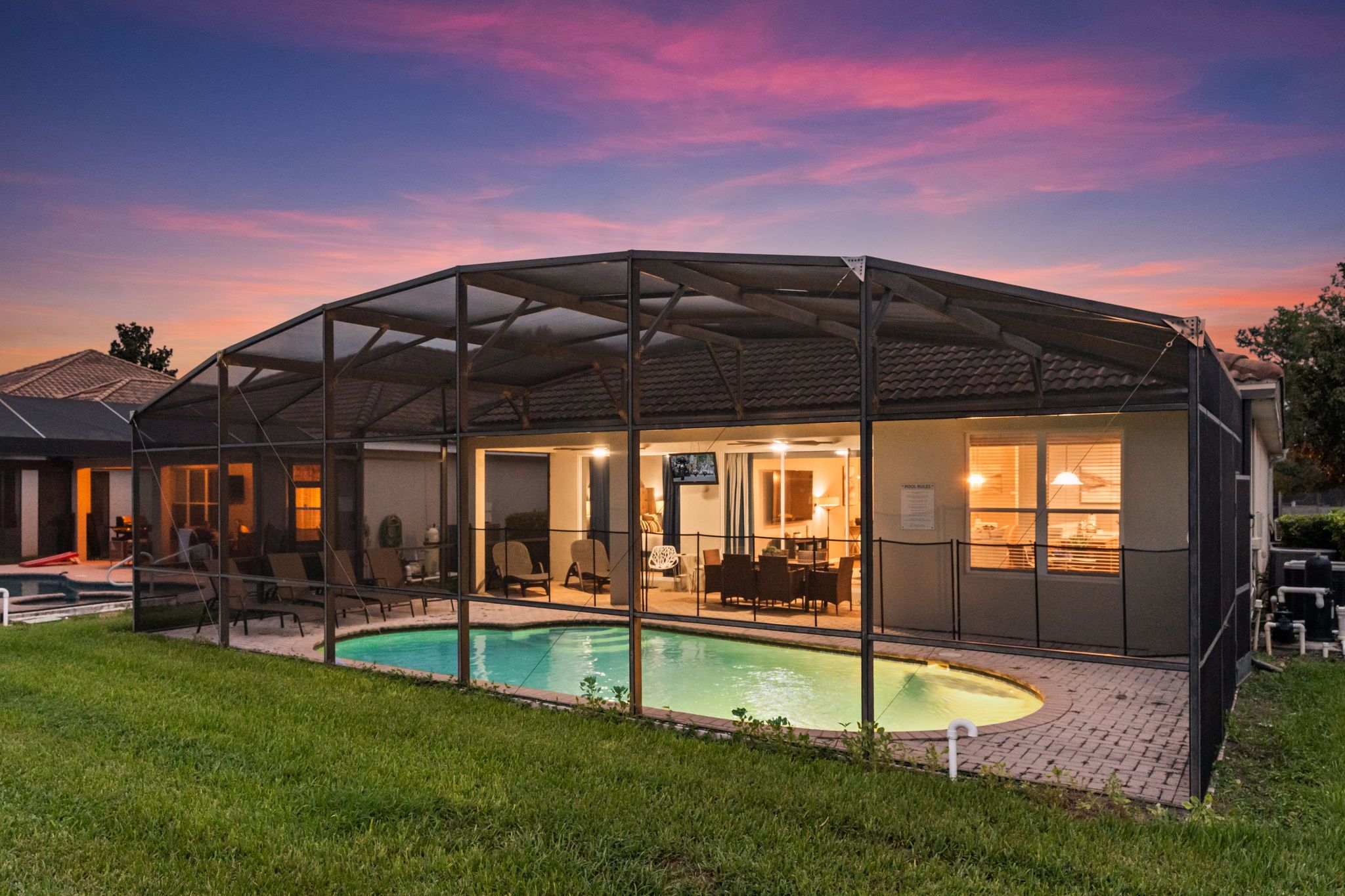 A covered outdoor pool area with a patio and seating, surrounded by a fence.
