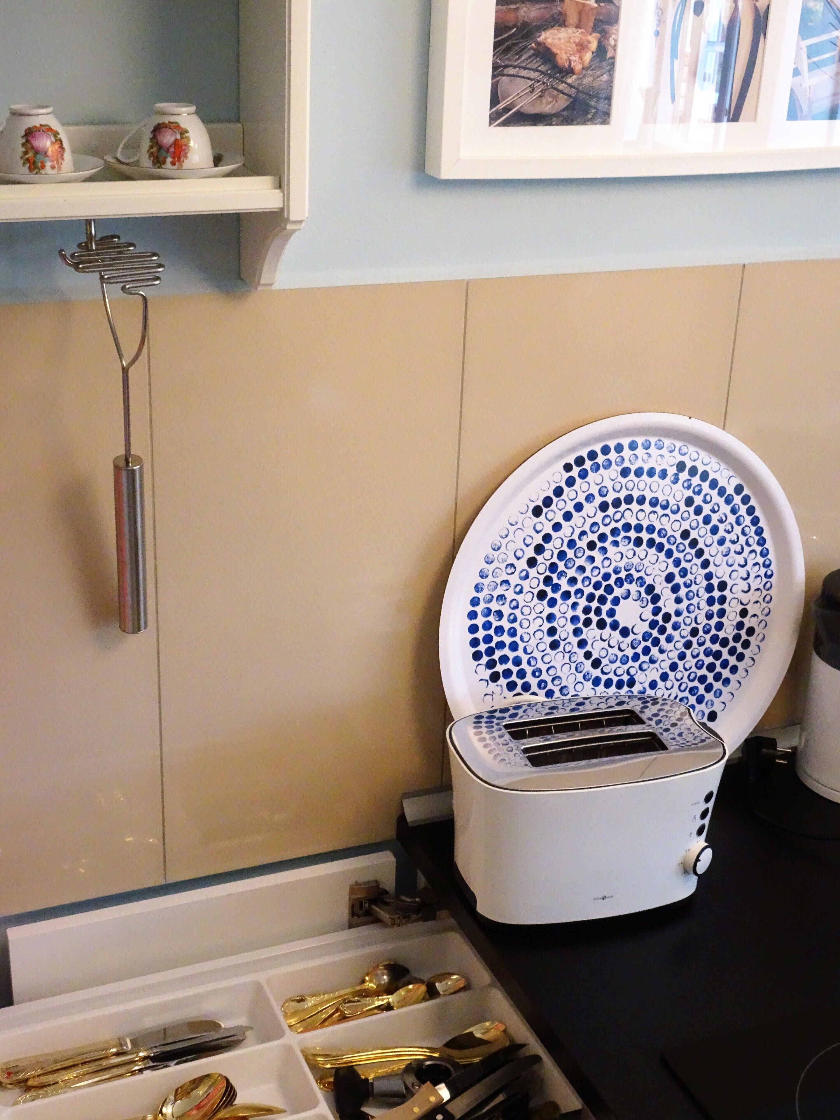 A kitchen with a toaster, a drawer with utensils, and a shelf with cups.