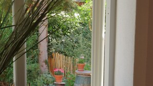 Een raam met uitzicht op een tuin, inclusief potplanten en een houten omheining.