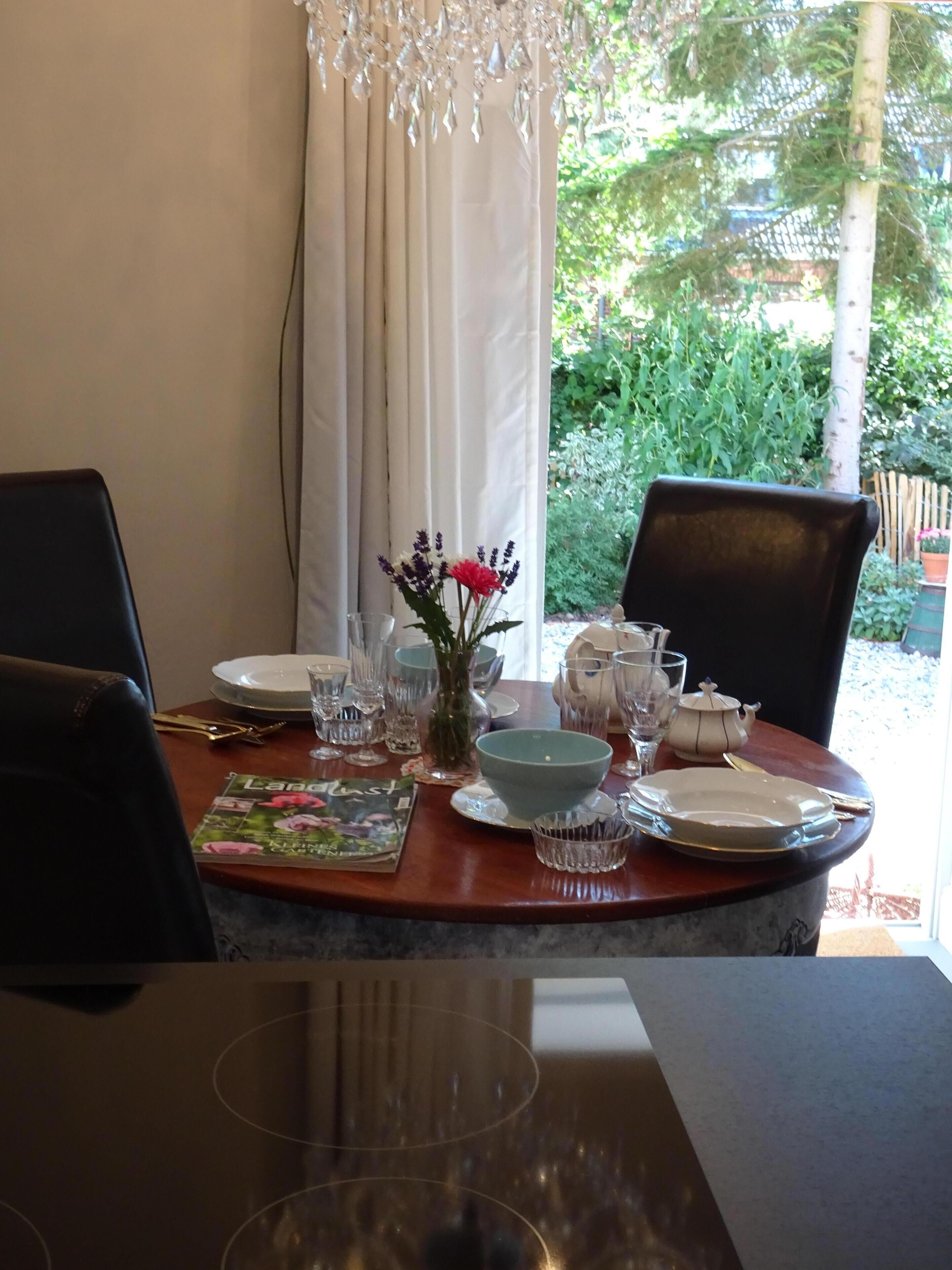 A dining table set with plates, glasses, and cutlery, a vase with flowers, and a chandelier.