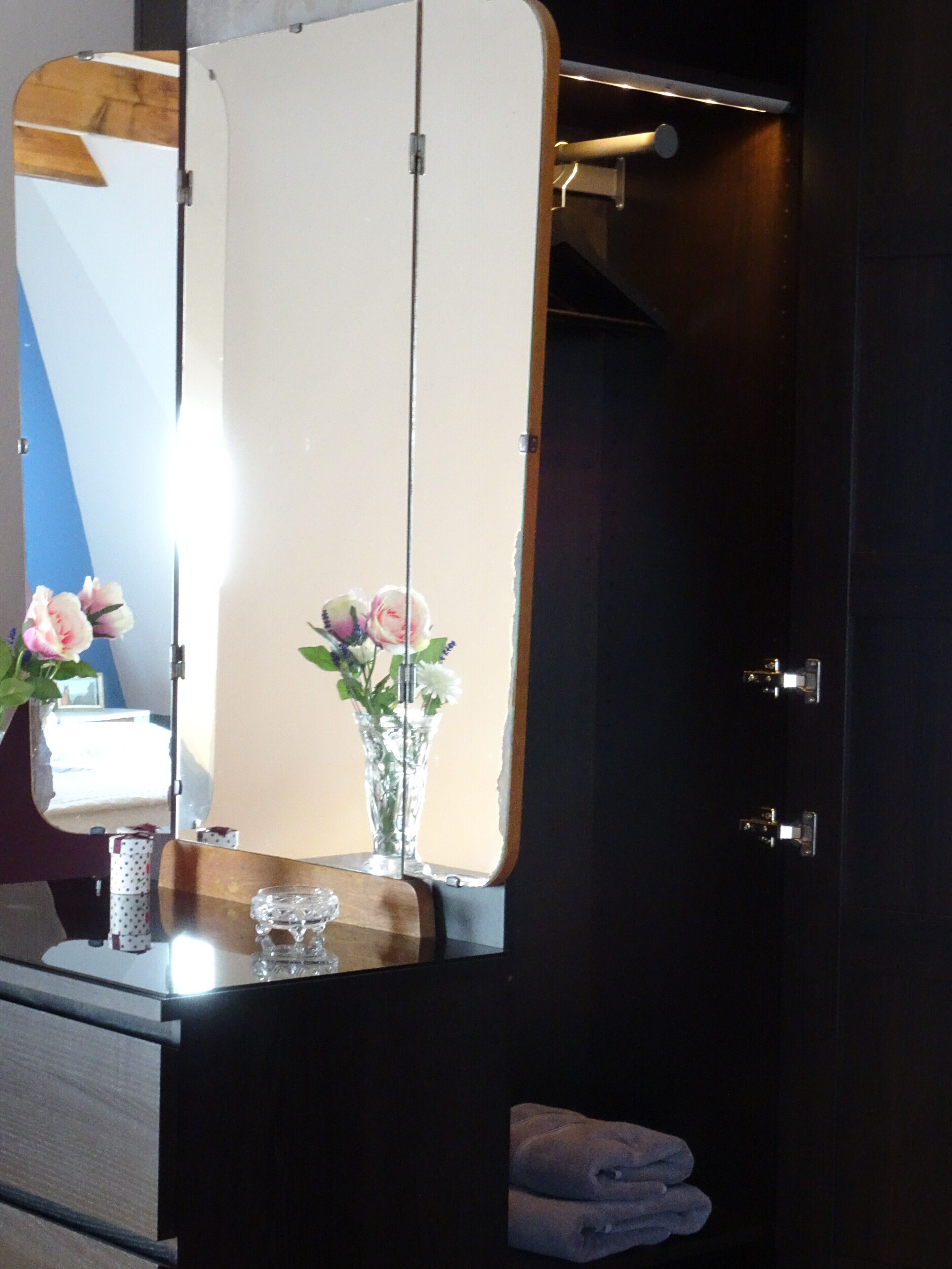 A bathroom with a large mirror, a vase with flowers, and a towel rack.