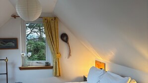 Un dormitorio con cama, mesita de noche, ventana con cortinas, lámpara colgante y un adorno en la pared.