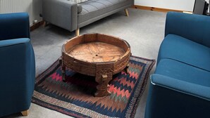 Una habitación tipo loft con un sofá gris, sillones azules, una mesa de centro de madera y una alfombra estampada.