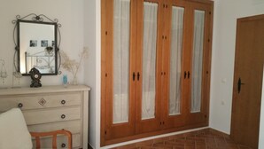 A room with a wooden wardrobe, a mirror with a decorative frame, a small table with a clock, and a chair. - HOUSE WITH PRIVATE PLOT - CONIL DE LA FRONTERA (FREE WIFI) (Conil de la Frontera)