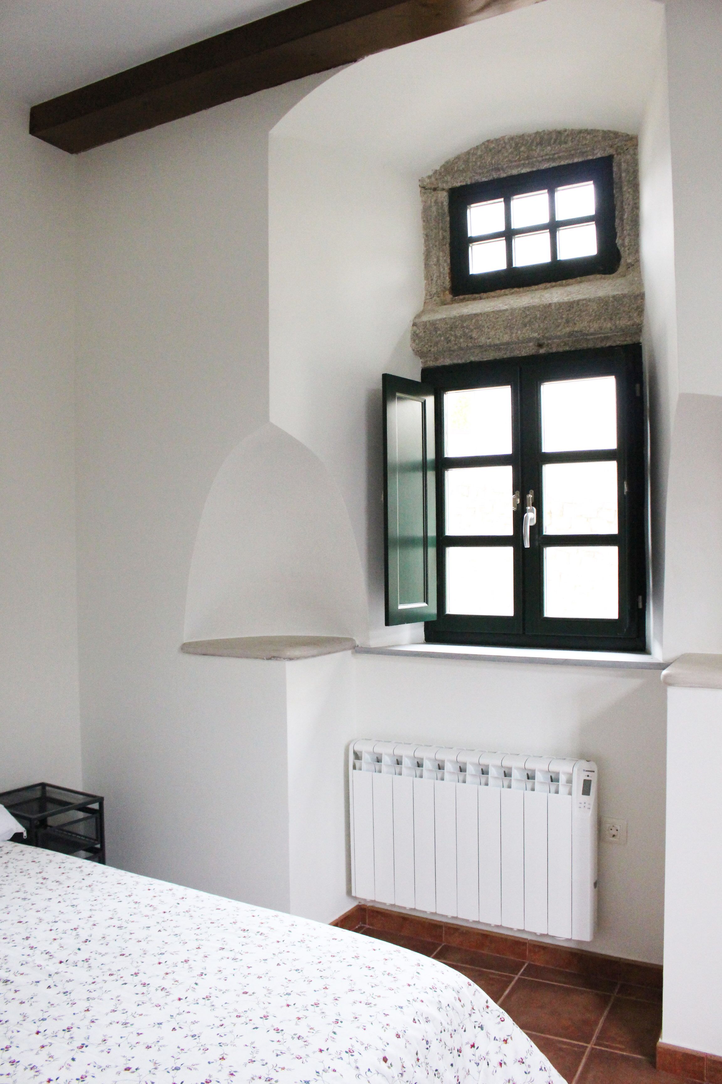 Een slaapkamer met een bed, een raam met een stenen vensterbank, en een witte radiator.