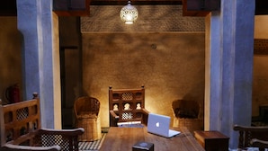 Un intérieur marocain traditionnel avec une table en bois, deux chaises en osier, un ordinateur portable et une lampe décorative.
