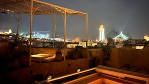 Une terrasse sur le toit, agrémentée d’une pergola, de plantes en pot et offrant une vue sur les bâtiments illuminés en arrière-plan.