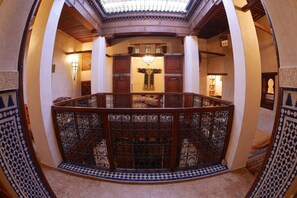 A spacious atrium with a high ceiling, a central wooden railing, and patterned floor tiles.