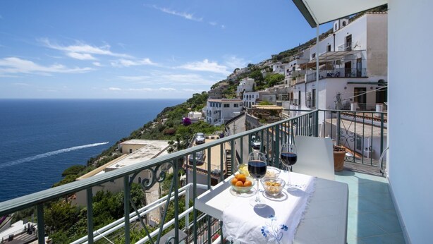 Ein Balkon mit Tisch für zwei Personen, mit Blick auf eine Küstenstadt, Gebäude und das Meer.