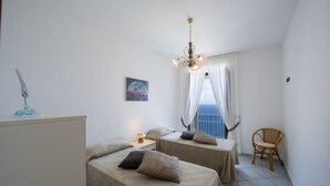 Ein Zimmer mit zwei Betten, einem Sessel, einem Nachttisch, einer Lampe, einem Bild und Meerblick.