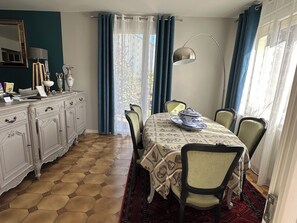 A dining area with a table set for four, a cabinet with decorative items, and a view through the window.