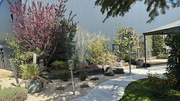 A garden pathway with a metal fence, potted plants, and a pergola structure. - LA VERANDA (VERDIGNY)