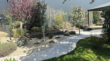 Un vialetto in giardino con recinzione in metallo, piante in vaso e una struttura a pergola.