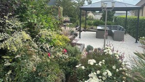 A garden patio with a pergola, seating area, and a variety of plants and flowers. - LA VERANDA (VERDIGNY)