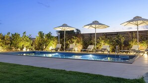 Une piscine rectangulaire, bordée d’une terrasse carrelée, entourée de chaises longues et de parasols.