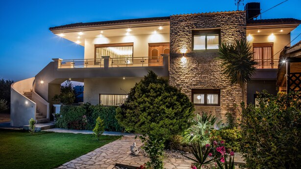 Une maison moderne à deux étages, dotée d’une façade en pierre, d’un balcon et d’un jardin bien aménagé et bien éclairé.