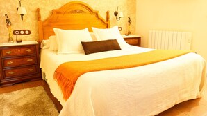 A neatly made bed with a wooden headboard, two bedside tables with lamps, a radiator, and a wooden coat rack. - ALZINA apartment in the heart of the Penedés. PB-00489 (Pontons)