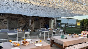 Een terras met eettafels gedekt voor het ontbijt, met brood, gebak en sinaasappelsap.