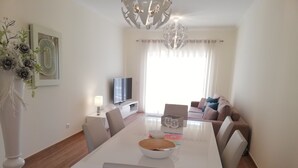 A modern living room with a dining table, chairs, a sofa, a TV, and a chandelier. - Beautiful new two bedroom apartment in Albufeira, Algarve<br> (Albufeira)