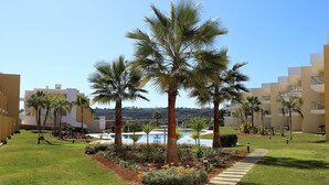 A well-maintained garden with palm trees, a swimming pool, and a clear sky. - Beautiful new two bedroom apartment in Albufeira, Algarve<br> (Albufeira)