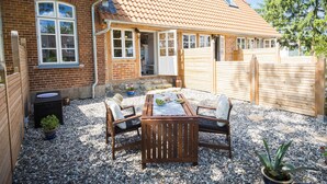 A patio with a wooden table and chairs, a brick house with a tiled roof, and a gravel ground. - stylish and nostalgic near Timmendorfer Strand Baltic Sea and old town Lübeck (Offendorf)