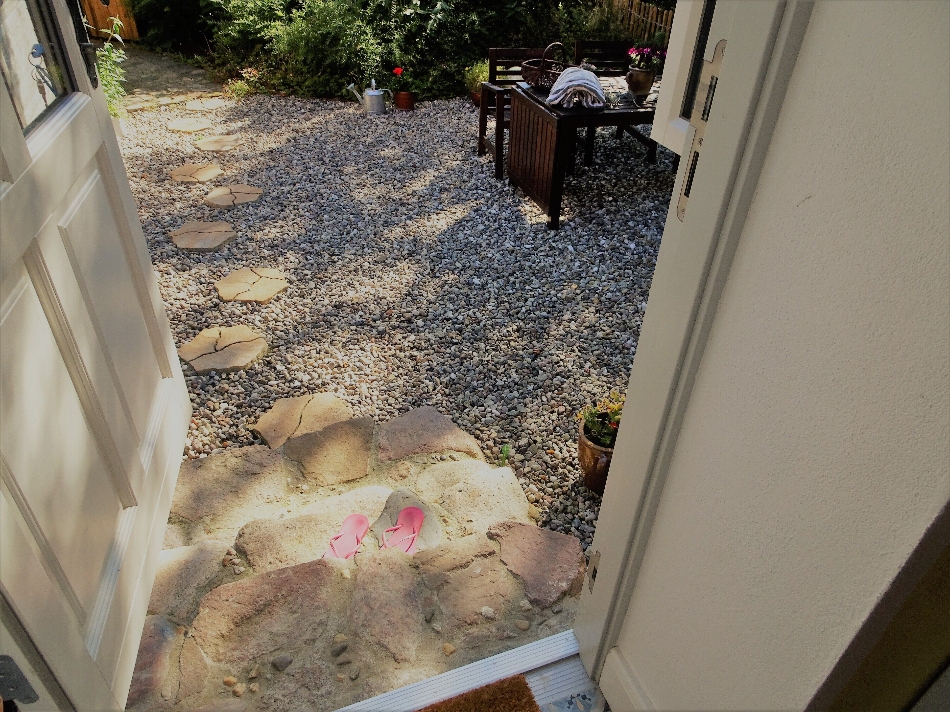 A stone pathway leading to a seating area with a table and chairs, surrounded by potted plants and a wooden fence.