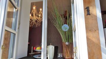An open door leading to a room with a chandelier, a vase with tall plants, and a wooden door with a brass handle.