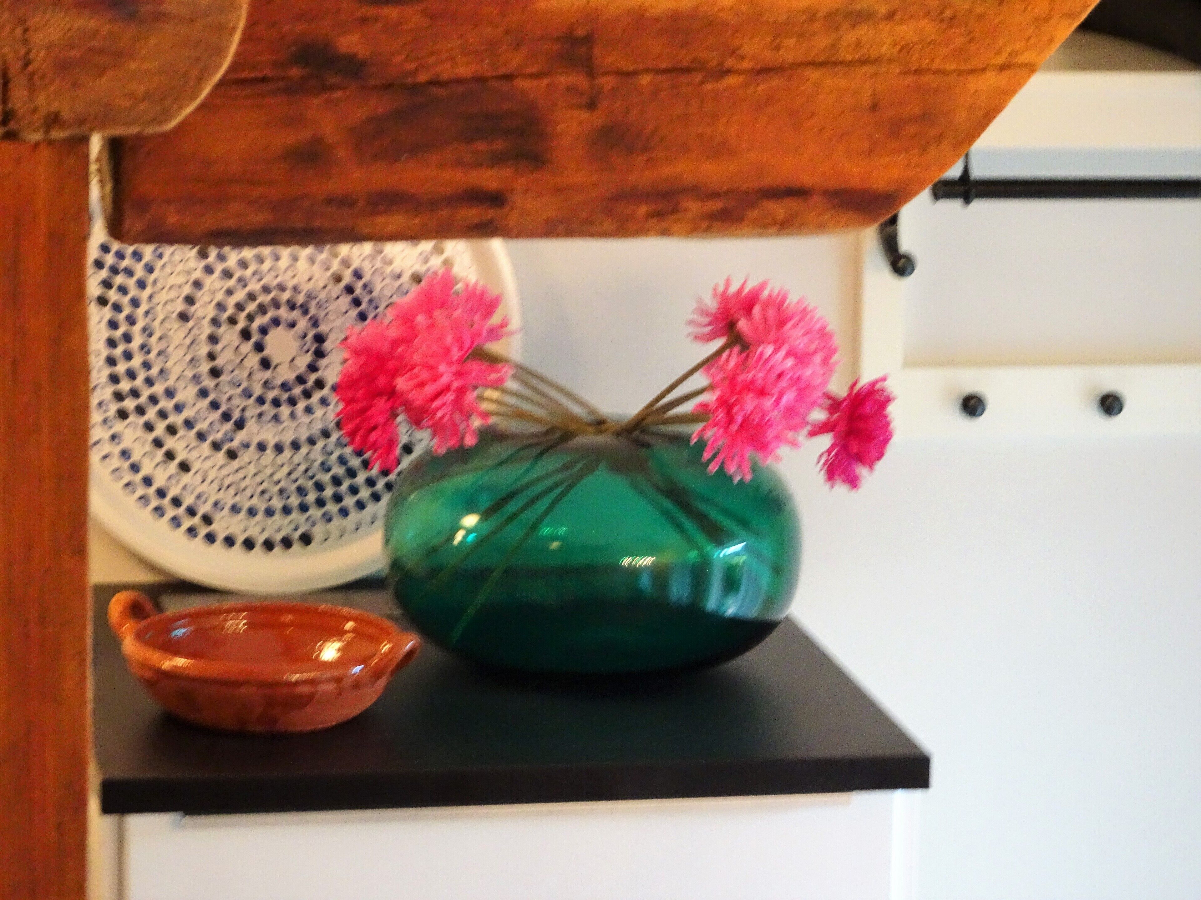 Eine grüne Vase mit rosa Blumen auf einer schwarzen Arbeitsplatte.