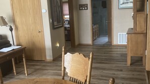 Un comedor con una mesa y sillas de madera, piso de madera y una puerta que da a otra habitación.