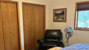 Un dormitorio con una cama, una silla, una mesa de madera y una ventana.