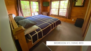 Un dormitorio con una cama tamaño king, paredes de madera, una mesita pequeña y una ventana con cortinas.