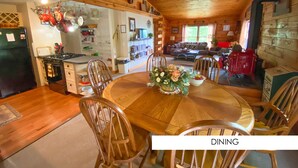 Un comedor de madera acogedor con una mesa redonda y sillas, una araña y una cocina visible al fondo.