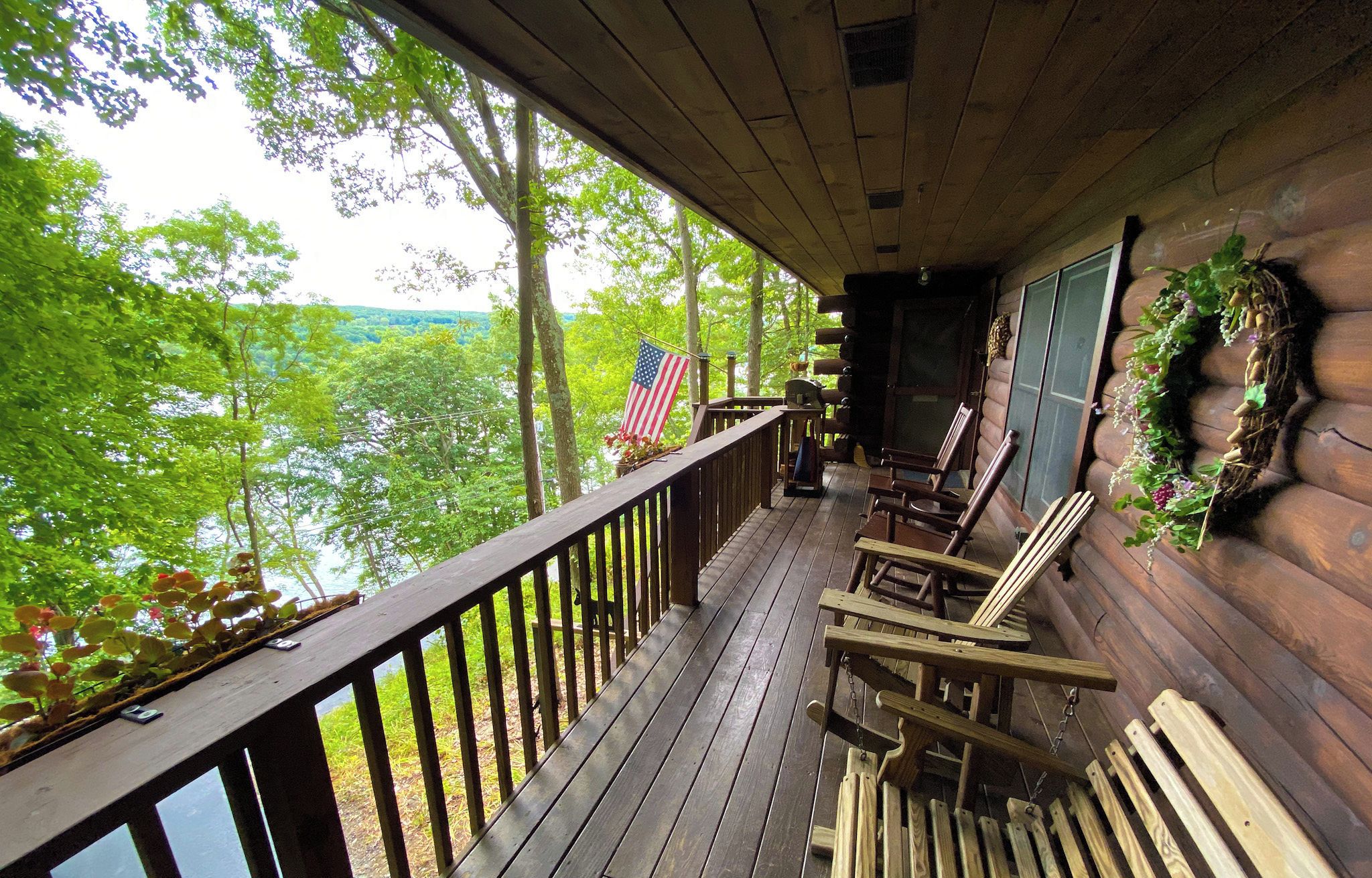 A front porch with a wooden railing, two rocking chairs, and a view of a forested area.